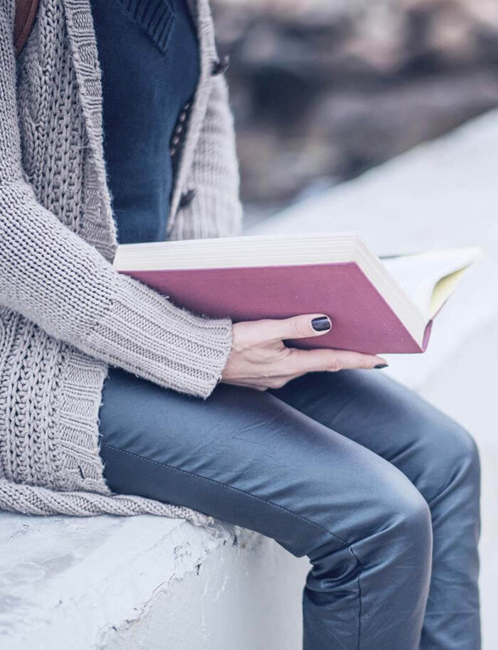 An older woman in a cardigan reading a book by the window